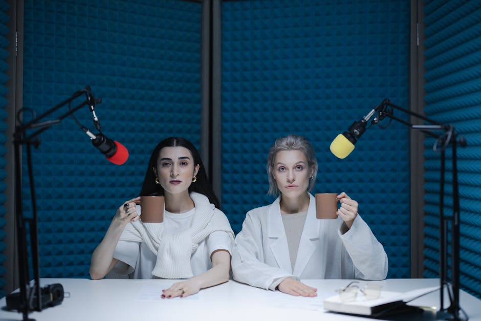 Two women in a soundproof podcast studio holding mugs next to microphones